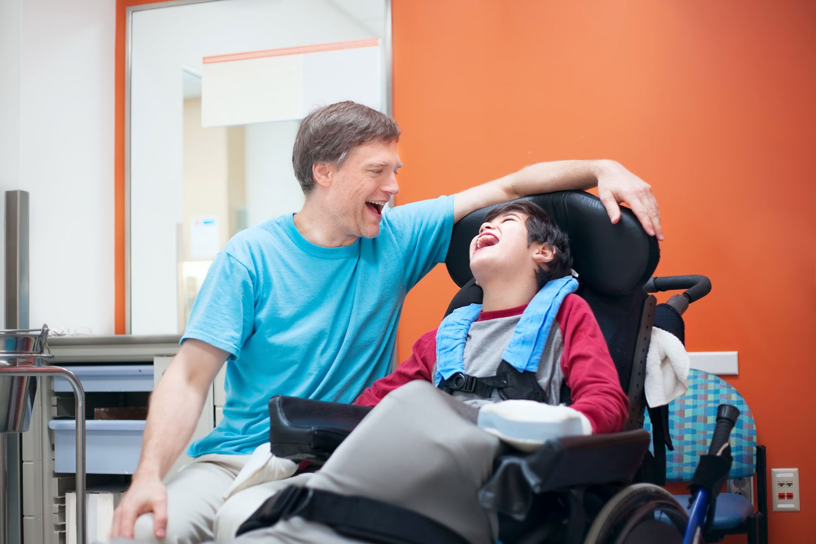 Boy in wheelchair laughing with male adult caregiver