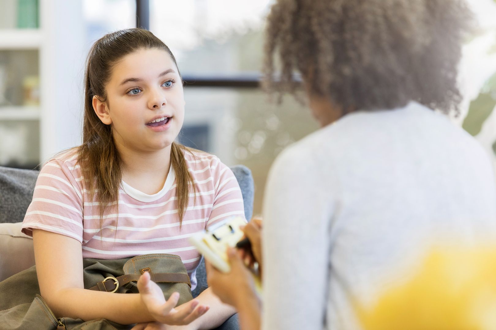 Young girl with ponytail talking to someone off camera with a neutral expression