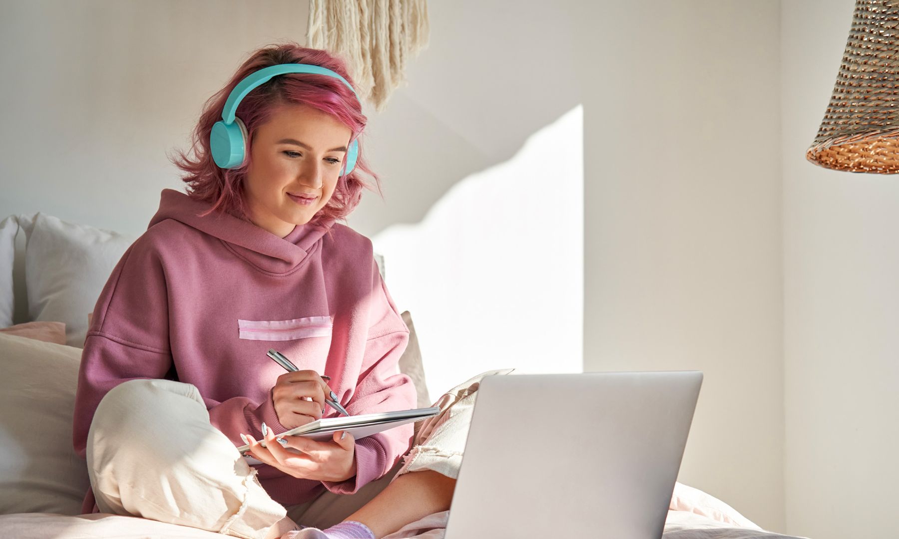 Teenage girl with pink hair in bedroom listening to music on mint green headphones